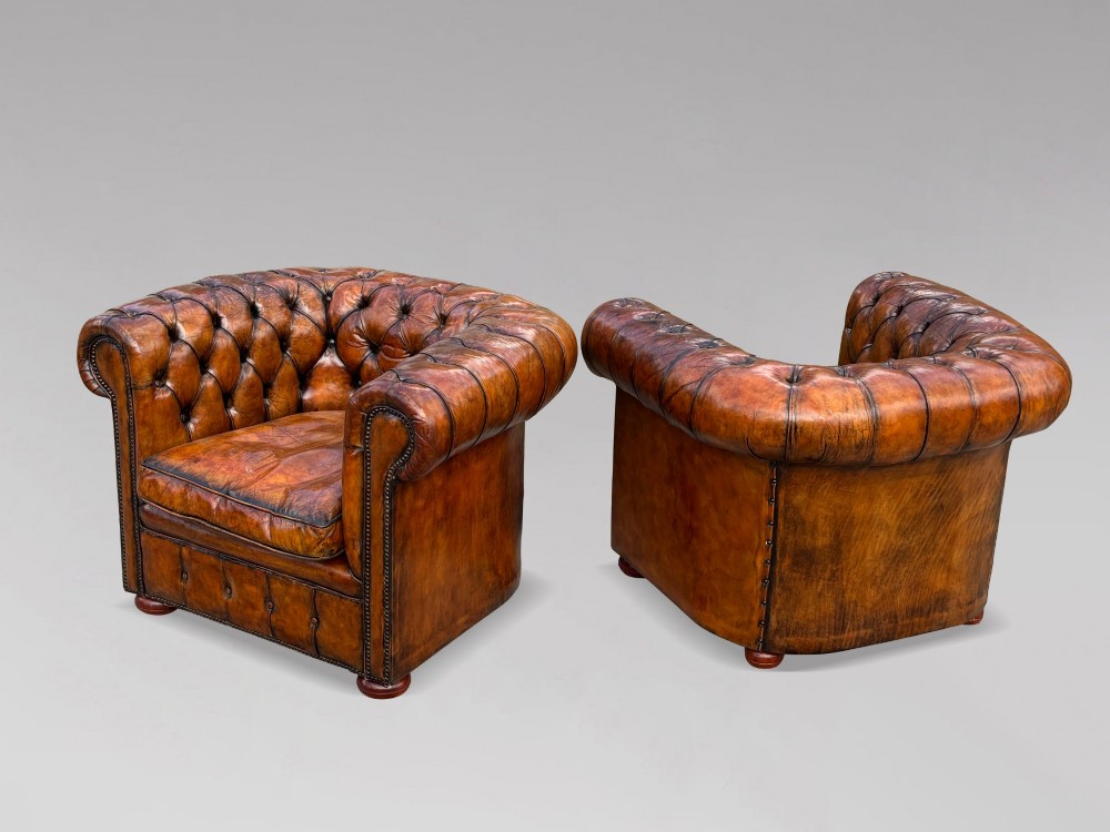 A pair of late Victorian deep-buttoned brown leather Chesterfield club armchairs with rolled arms, brass studding, and turned wooden feet. View IV