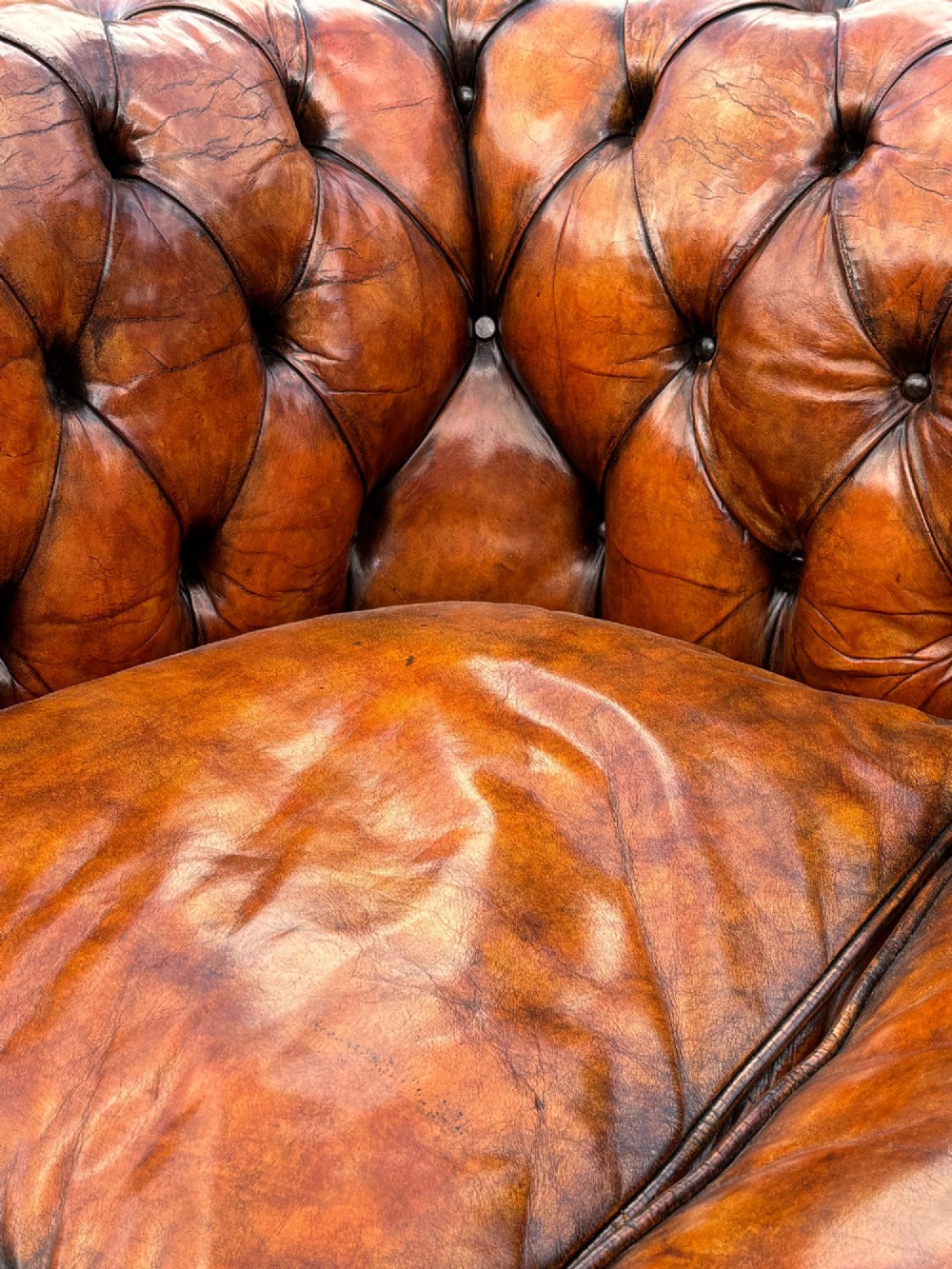 A pair of late Victorian deep-buttoned brown leather Chesterfield club armchairs with rolled arms, brass studding, and turned wooden feet. View V