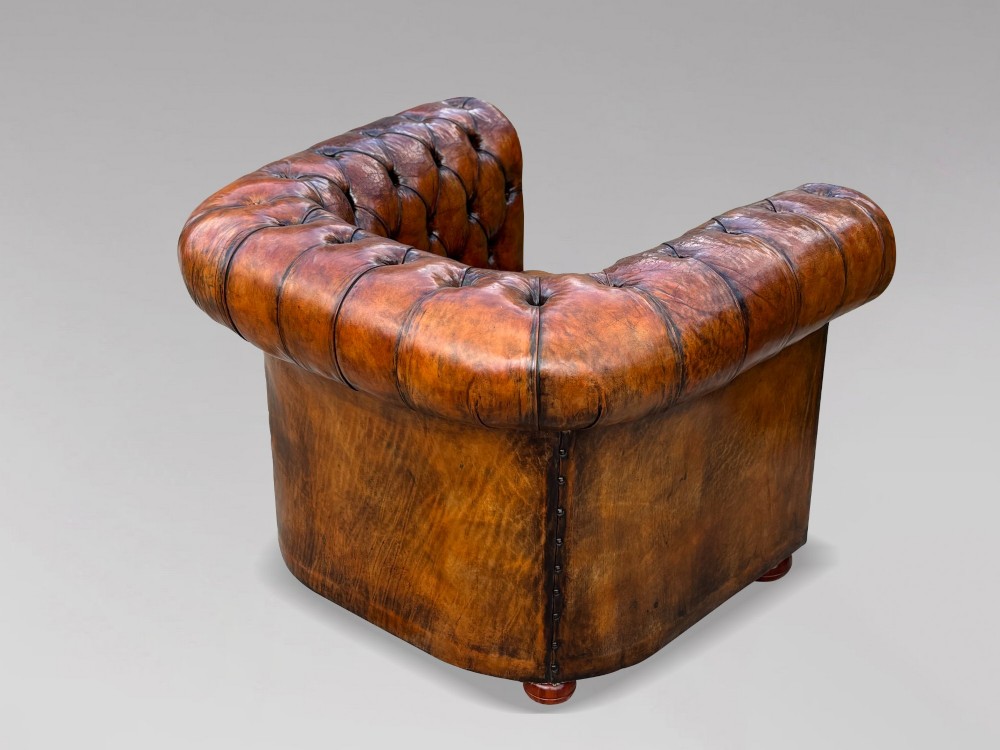 A pair of late Victorian deep-buttoned brown leather Chesterfield club armchairs with rolled arms, brass studding, and turned wooden feet. View VI