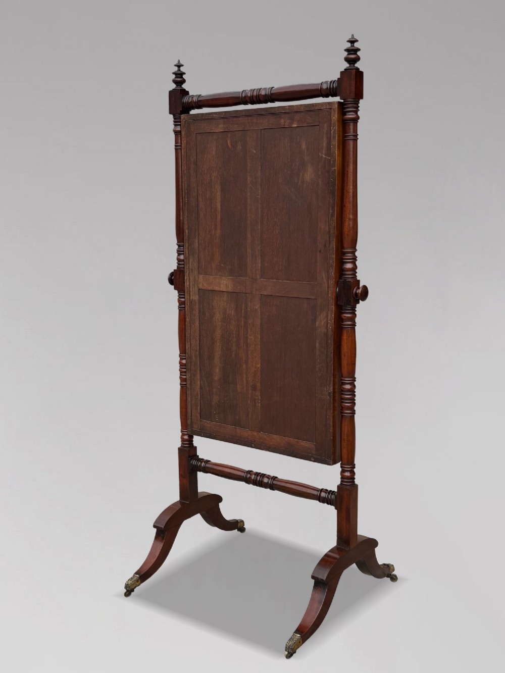 An early 19th-century Regency mahogany cheval mirror featuring turned uprights, brass candle sconces, finials, and splayed legs on brass castors. View III