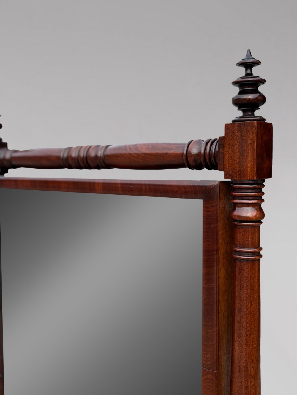 An early 19th-century Regency mahogany cheval mirror featuring turned uprights, brass candle sconces, finials, and splayed legs on brass castors. View IV