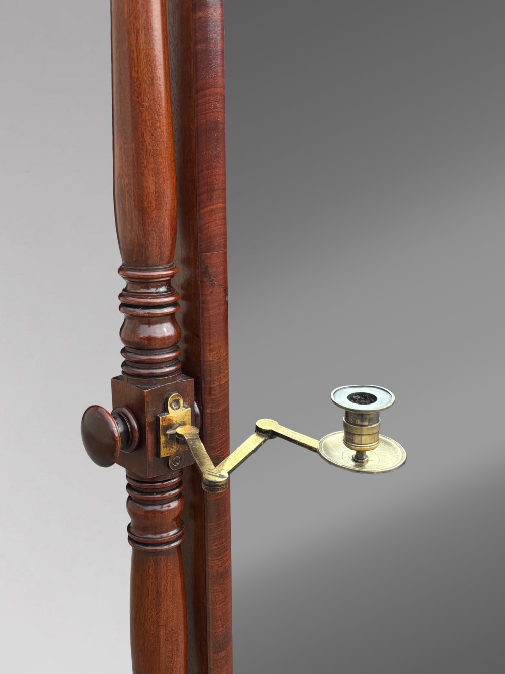 An early 19th-century Regency mahogany cheval mirror featuring turned uprights, brass candle sconces, finials, and splayed legs on brass castors. View V