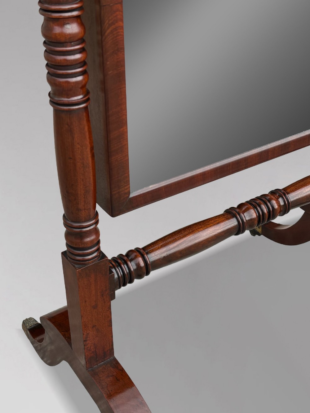 An early 19th-century Regency mahogany cheval mirror featuring turned uprights, brass candle sconces, finials, and splayed legs on brass castors. View VII