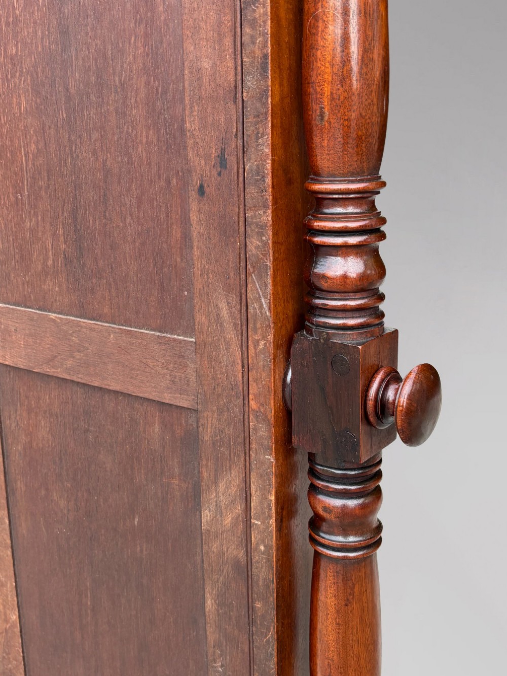 An early 19th-century Regency mahogany cheval mirror featuring turned uprights, brass candle sconces, finials, and splayed legs on brass castors. View VIII