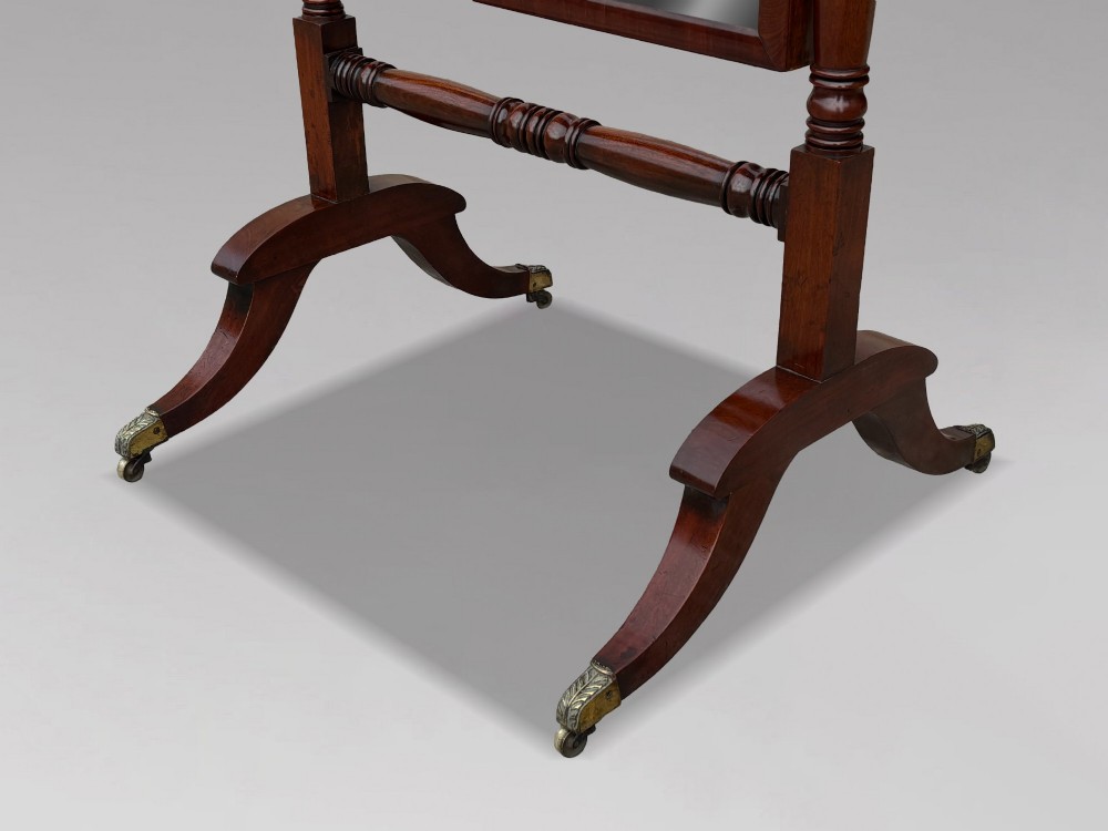 An early 19th-century Regency mahogany cheval mirror featuring turned uprights, brass candle sconces, finials, and splayed legs on brass castors. View XII