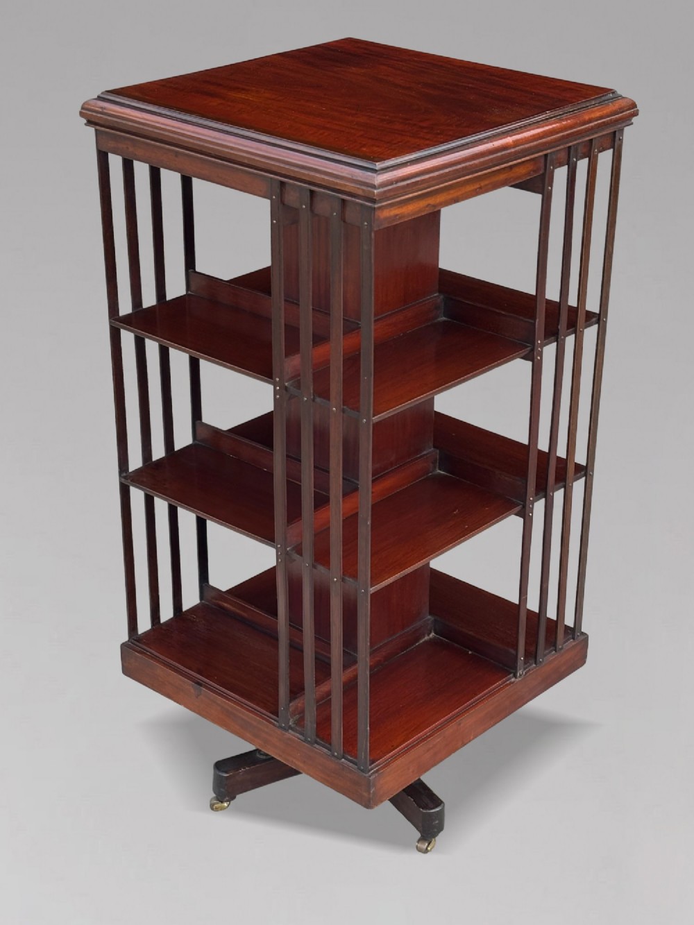 A four-tier Victorian mahogany revolving bookcase featuring vertical slatted sides, a square top, and a rotating base on brass castors.