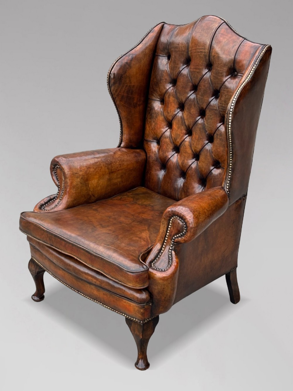 A 19th-century Victorian wingback armchair upholstered in deep-buttoned warm brown leather with brass stud detailing and carved mahogany legs. View II