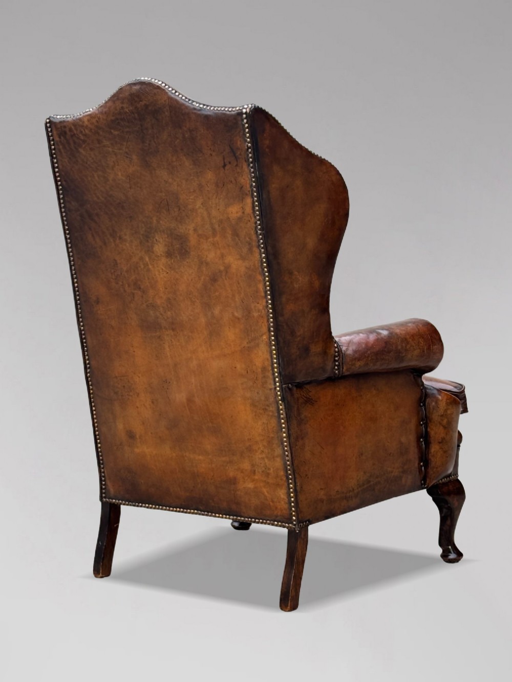 A 19th-century Victorian wingback armchair upholstered in deep-buttoned warm brown leather with brass stud detailing and carved mahogany legs. View III