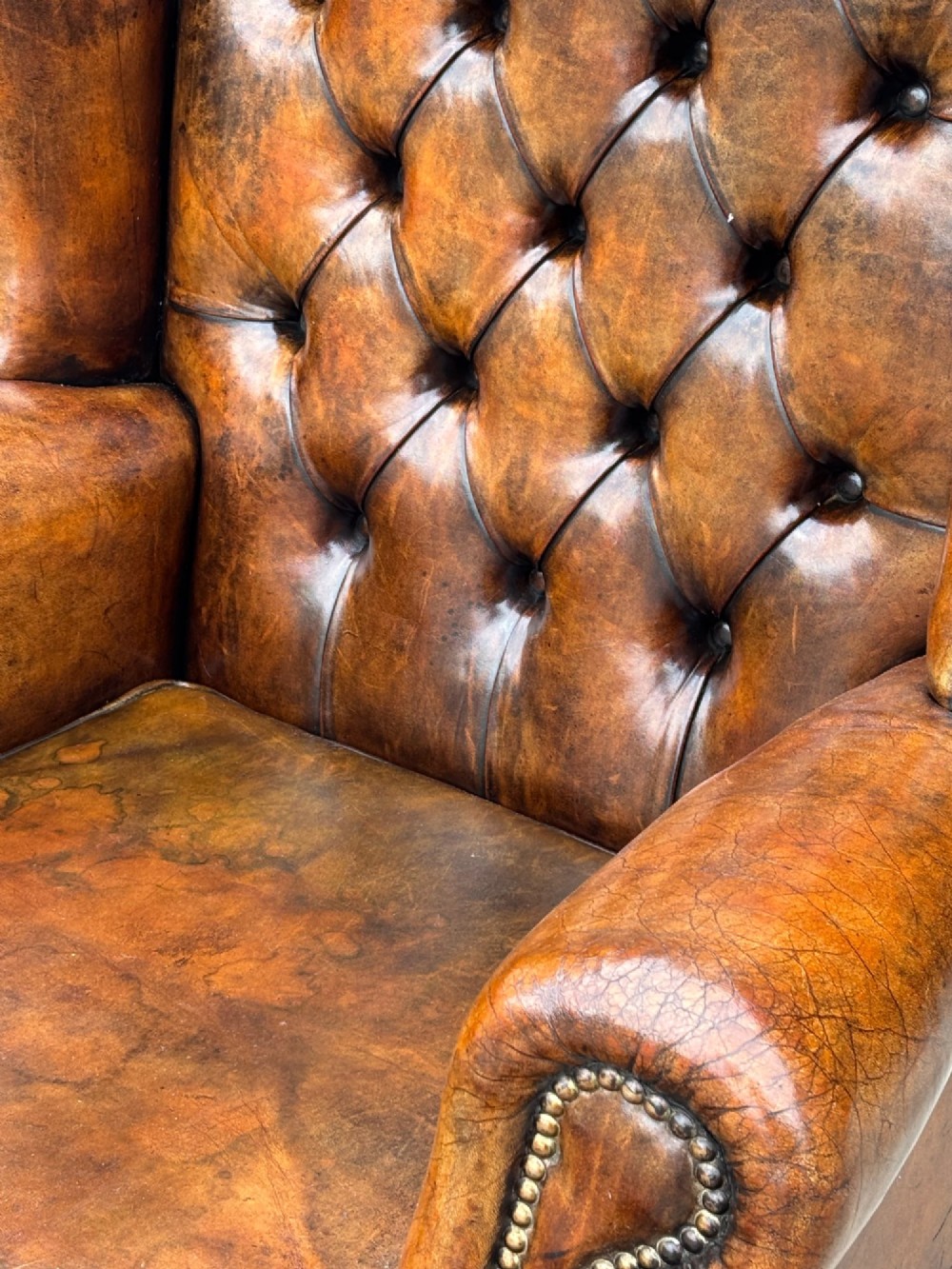 A 19th-century Victorian wingback armchair upholstered in deep-buttoned warm brown leather with brass stud detailing and carved mahogany legs. View IV