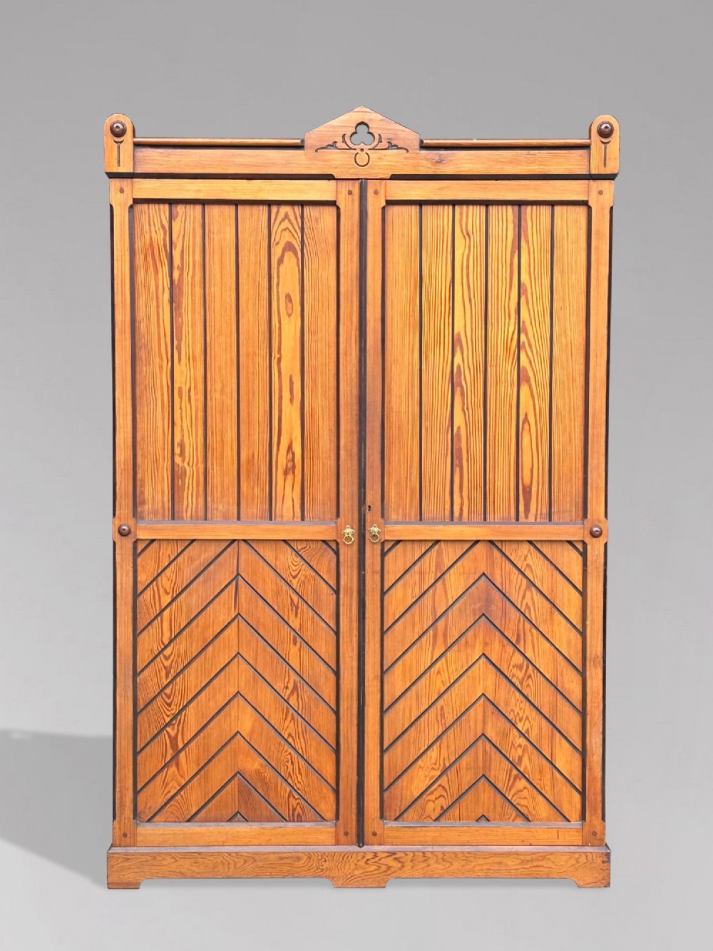 A late 19th-century pitch pine Arts and Crafts wardrobe featuring vertical slatted upper door panels, chevron lower panels, and a carved cresting rail. View II