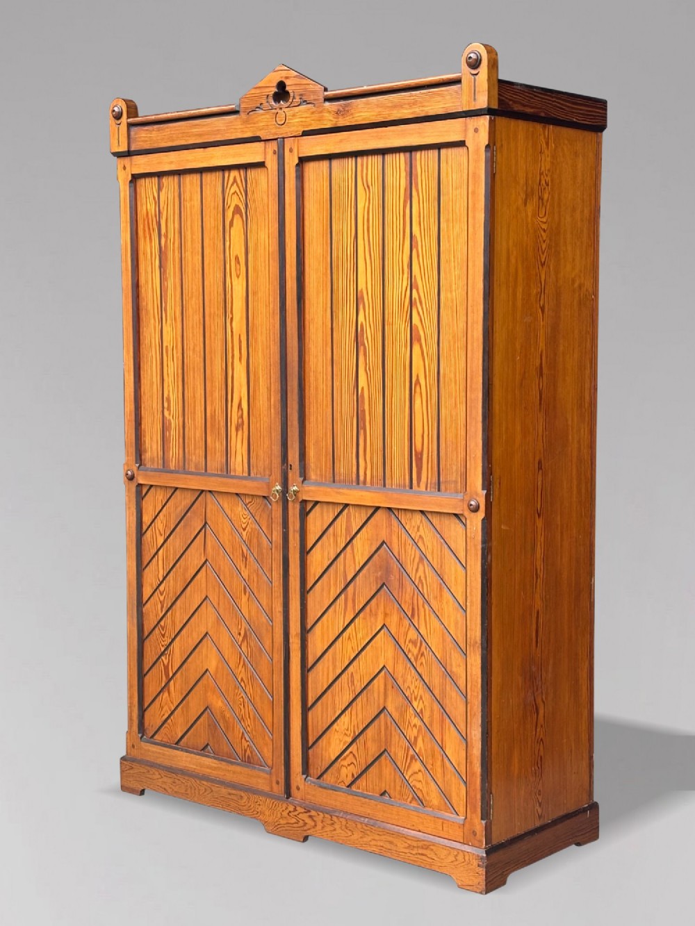 A late 19th-century pitch pine Arts and Crafts wardrobe featuring vertical slatted upper door panels, chevron lower panels, and a carved cresting rail. View III