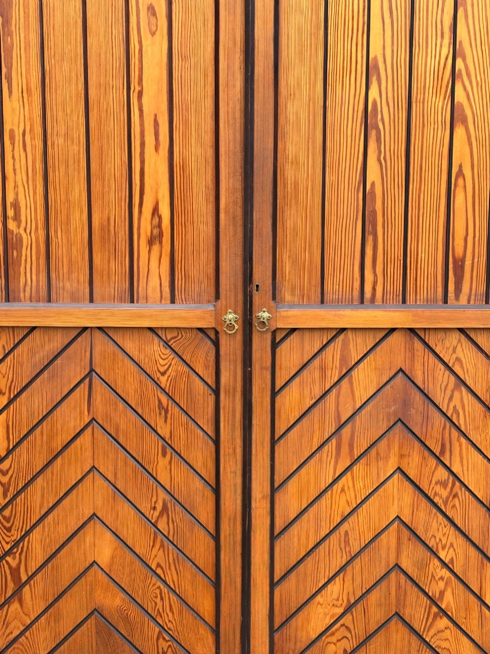 A late 19th-century pitch pine Arts and Crafts wardrobe featuring vertical slatted upper door panels, chevron lower panels, and a carved cresting rail. View IV