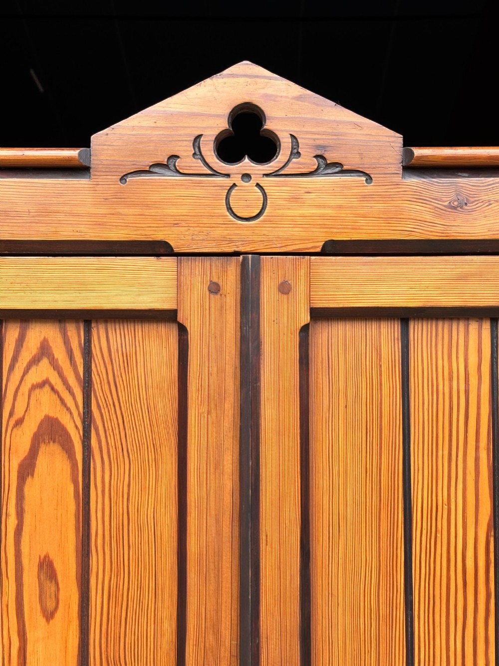 A late 19th-century pitch pine Arts and Crafts wardrobe featuring vertical slatted upper door panels, chevron lower panels, and a carved cresting rail. View V