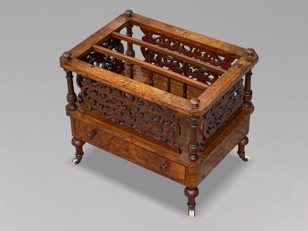 A mid-19th-century Victorian walnut music canterbury featuring open fretwork dividers, turned corner columns, a single base drawer, and turned legs with ceramic castors. View V