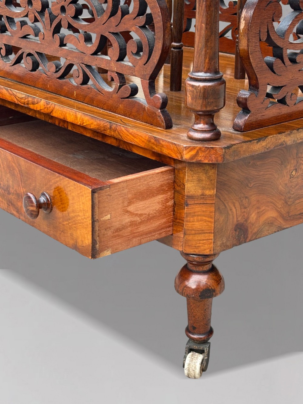A mid-19th-century Victorian walnut music canterbury featuring open fretwork dividers, turned corner columns, a single base drawer, and turned legs with ceramic castors. View VII