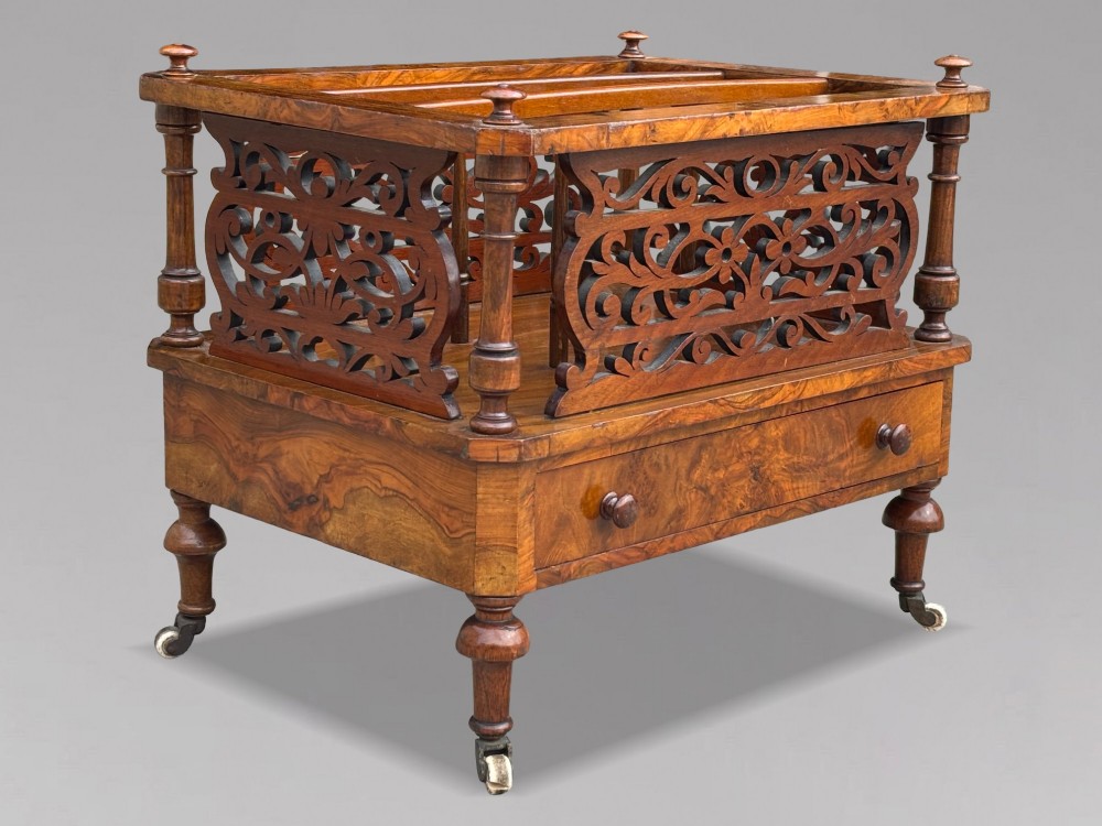 A mid-19th-century Victorian walnut music canterbury featuring open fretwork dividers, turned corner columns, a single base drawer, and turned legs with ceramic castors. View X