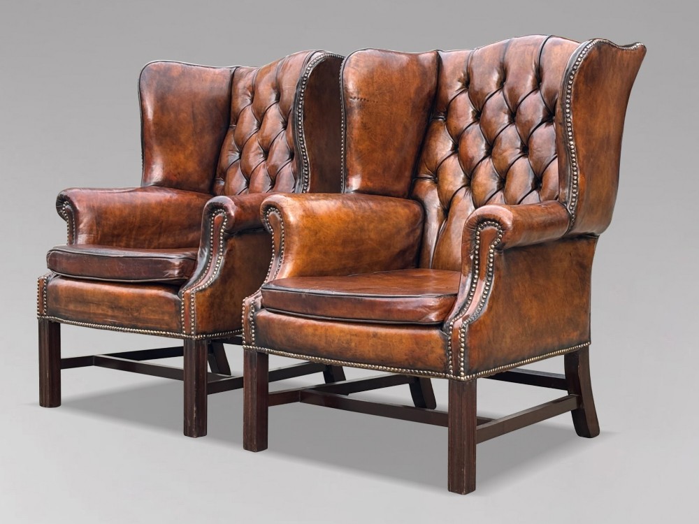 A pair of late Victorian wingback armchairs upholstered in deep-buttoned tan brown leather with brass stud trimming and dark wooden legs. View II