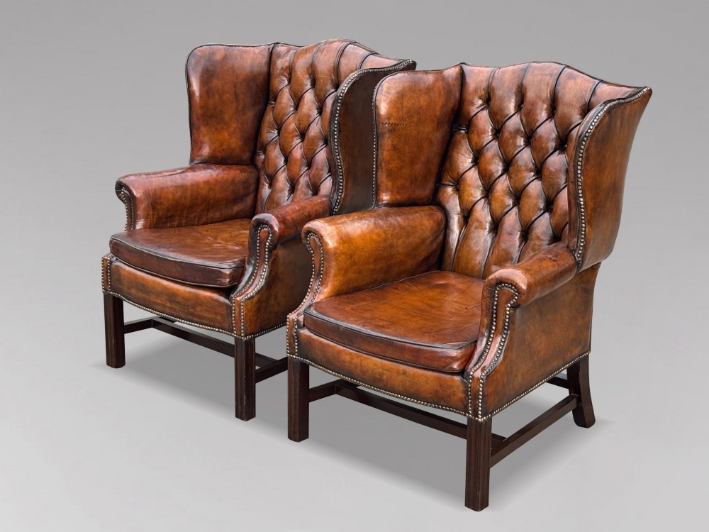 A pair of late Victorian wingback armchairs upholstered in deep-buttoned tan brown leather with brass stud trimming and dark wooden legs. View III