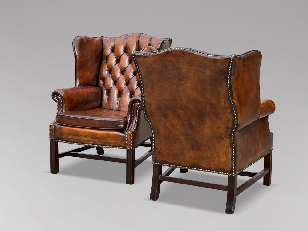A pair of late Victorian wingback armchairs upholstered in deep-buttoned tan brown leather with brass stud trimming and dark wooden legs. View IV