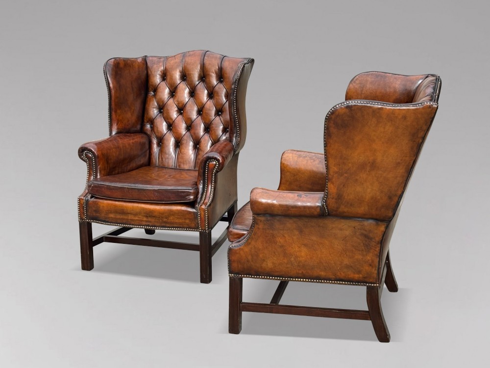 A pair of late Victorian wingback armchairs upholstered in deep-buttoned tan brown leather with brass stud trimming and dark wooden legs. View V