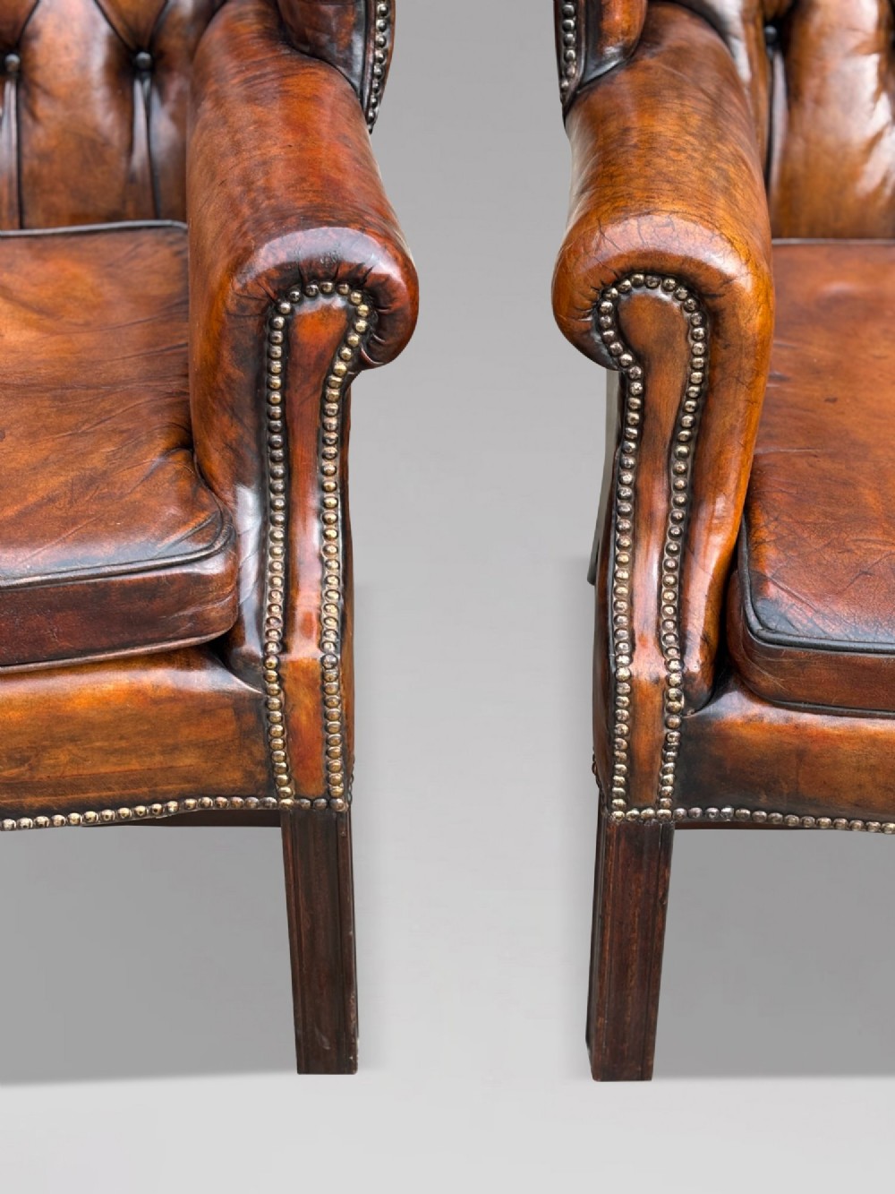 A pair of late Victorian wingback armchairs upholstered in deep-buttoned tan brown leather with brass stud trimming and dark wooden legs. View VI