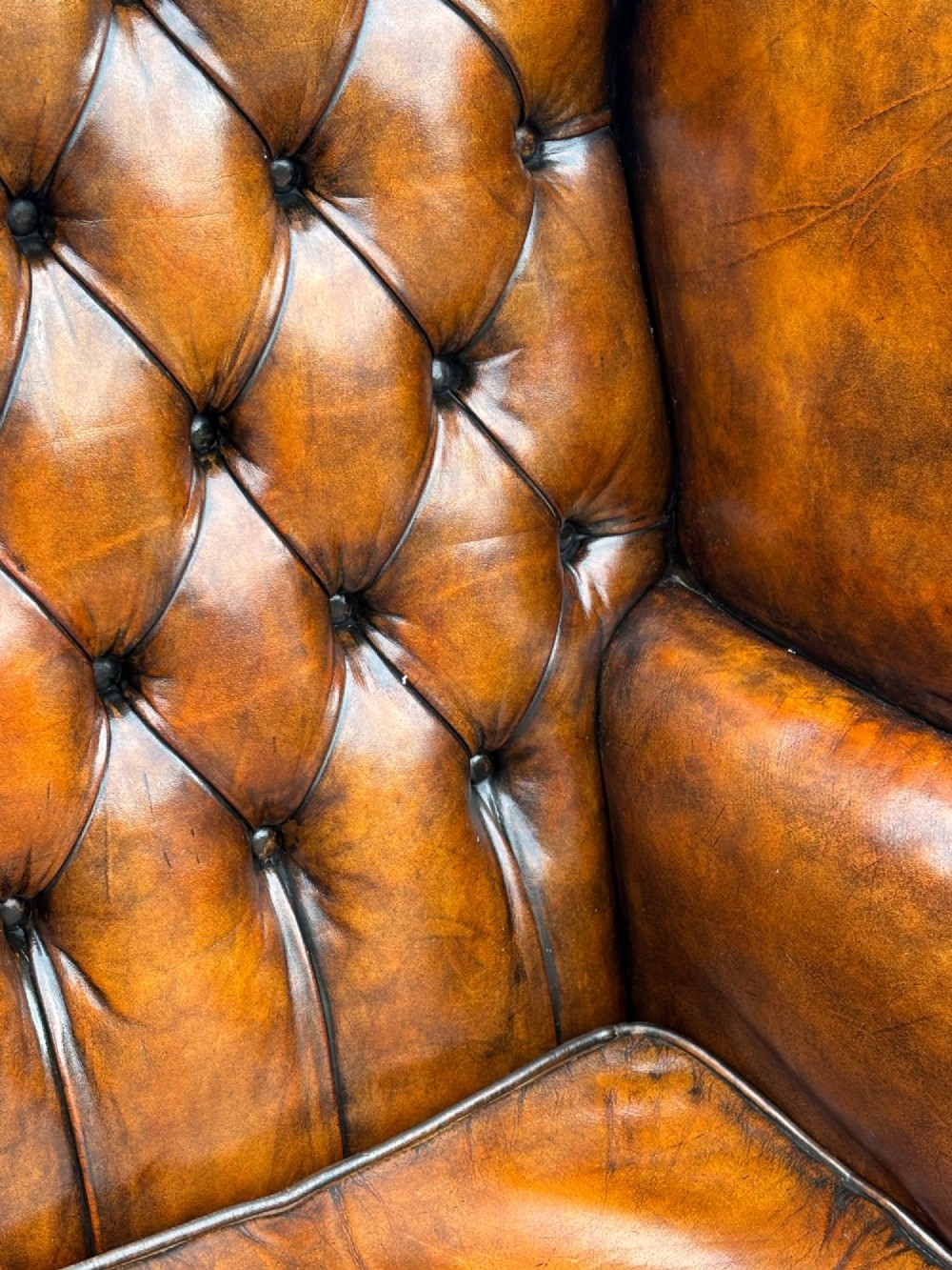 A pair of late Victorian wingback armchairs upholstered in deep-buttoned tan brown leather with brass stud trimming and dark wooden legs. View VII