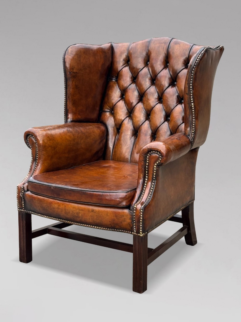 A pair of late Victorian wingback armchairs upholstered in deep-buttoned tan brown leather with brass stud trimming and dark wooden legs. View VIII