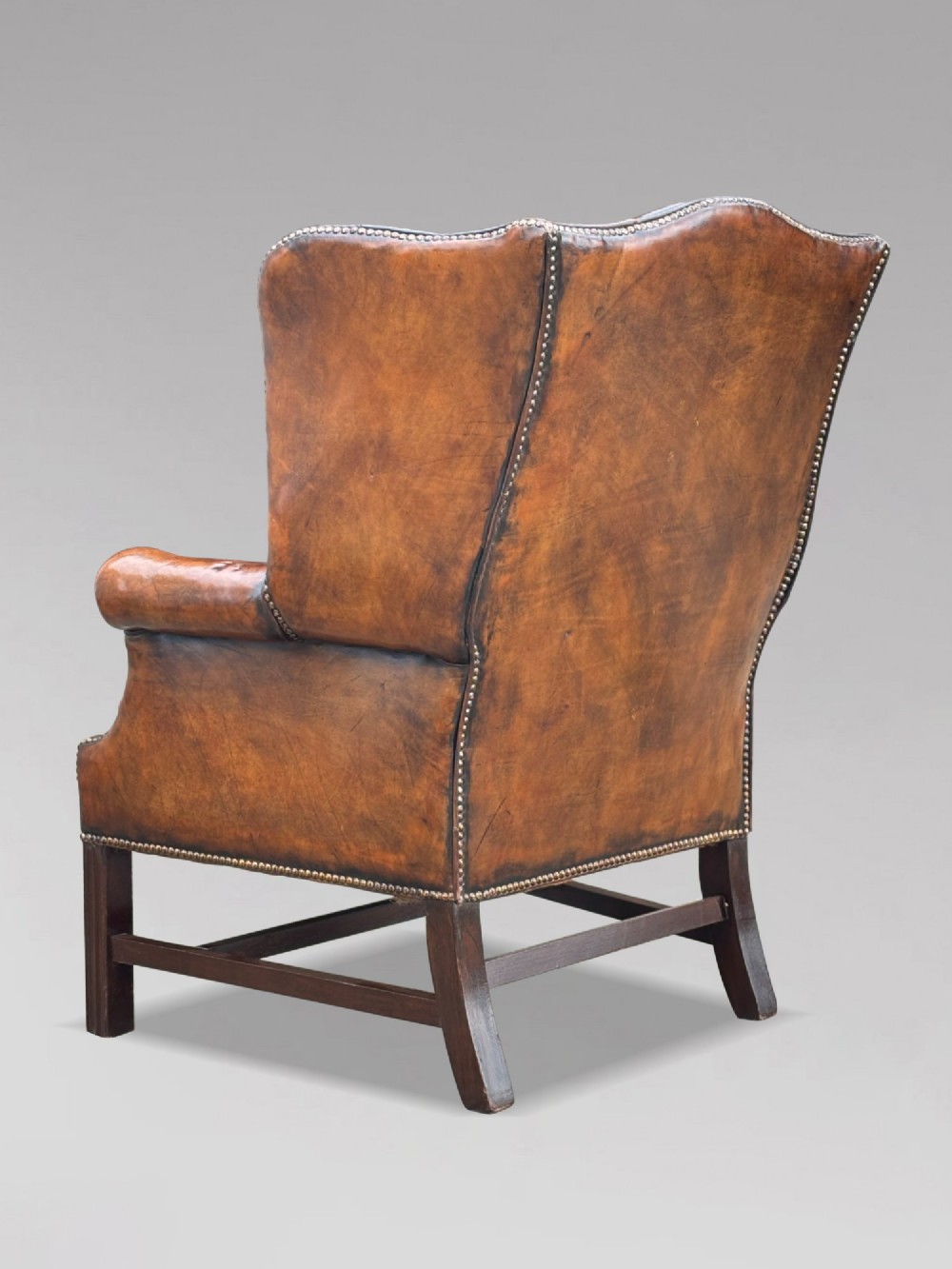 A pair of late Victorian wingback armchairs upholstered in deep-buttoned tan brown leather with brass stud trimming and dark wooden legs. View IX