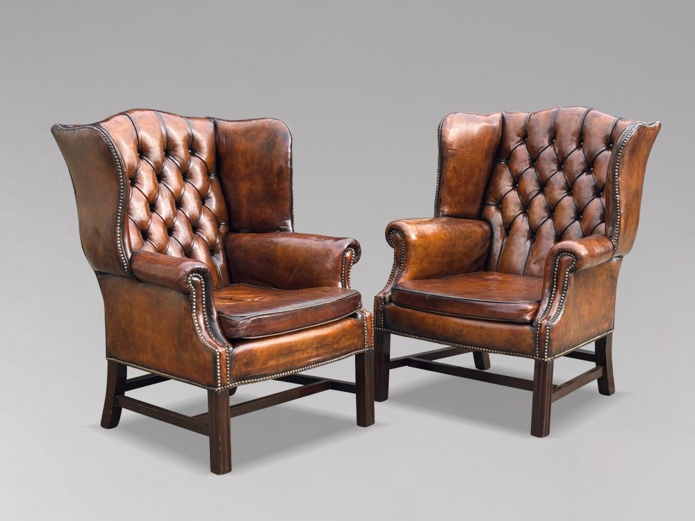 A pair of late Victorian wingback armchairs upholstered in deep-buttoned tan brown leather with brass stud trimming and dark wooden legs. View X