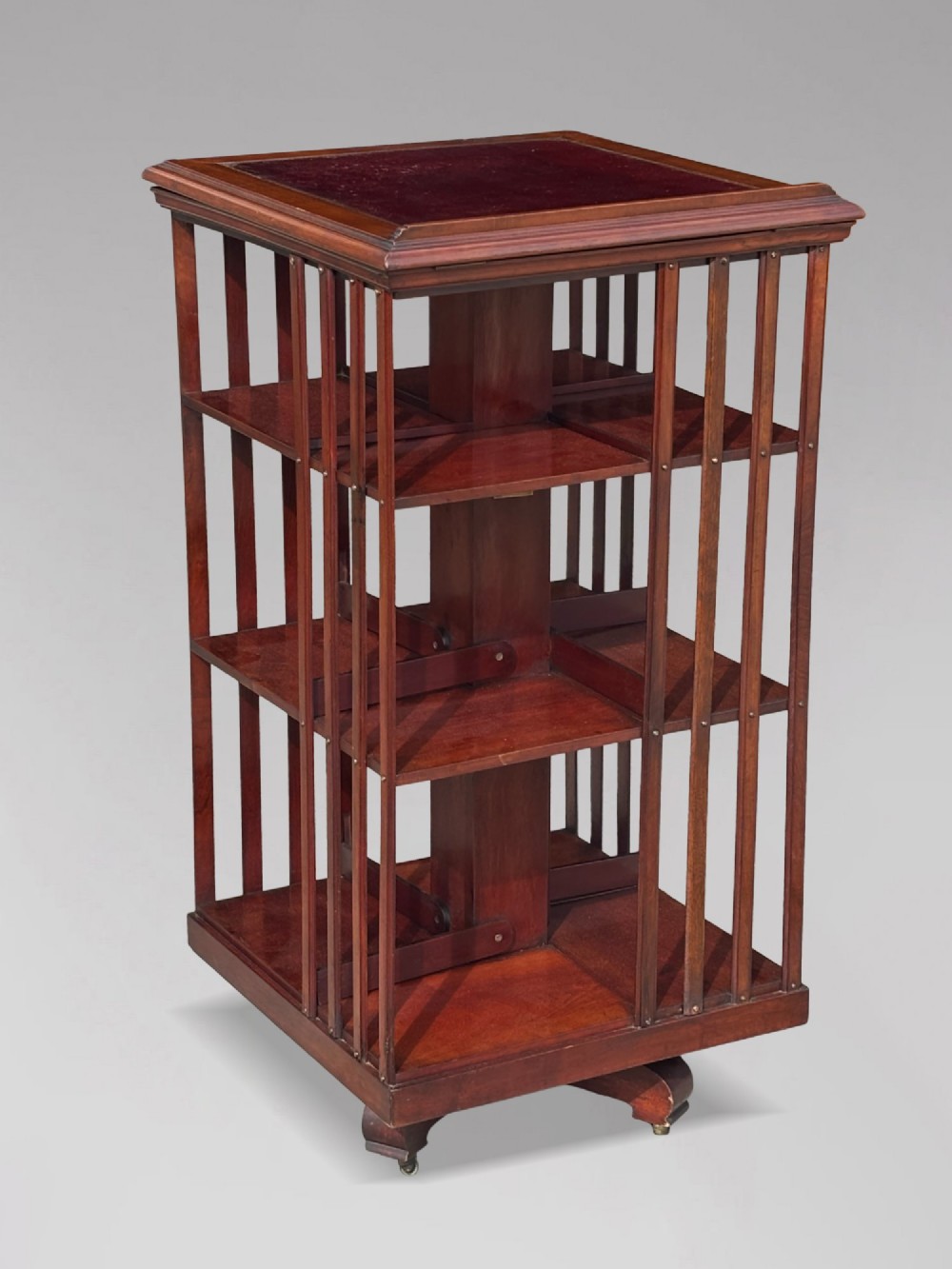 A tall nineteenth-century mahogany revolving bookcase featuring open slatted sides, tiered shelving, pull-out circular trays, and an angled reading slope with a burgundy leather surface. View II