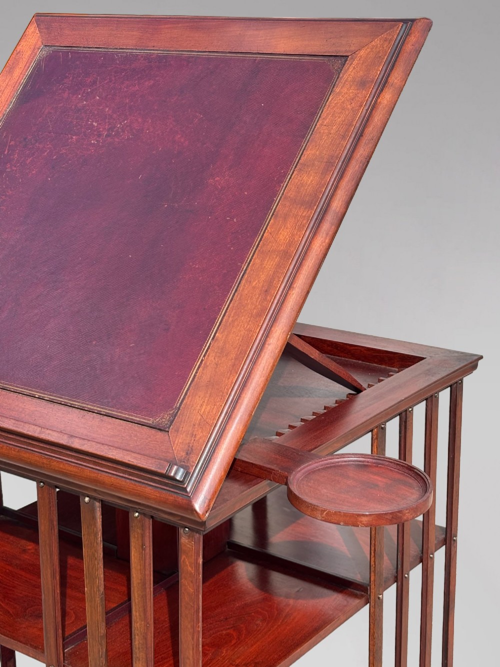 A tall nineteenth-century mahogany revolving bookcase featuring open slatted sides, tiered shelving, pull-out circular trays, and an angled reading slope with a burgundy leather surface. View VI