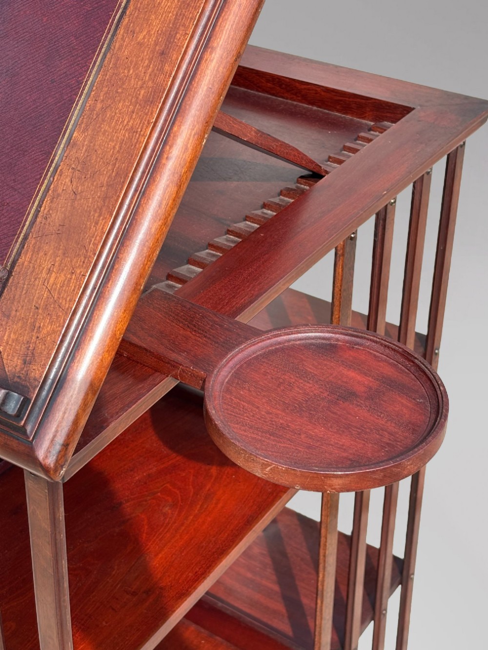 A tall nineteenth-century mahogany revolving bookcase featuring open slatted sides, tiered shelving, pull-out circular trays, and an angled reading slope with a burgundy leather surface. View VII