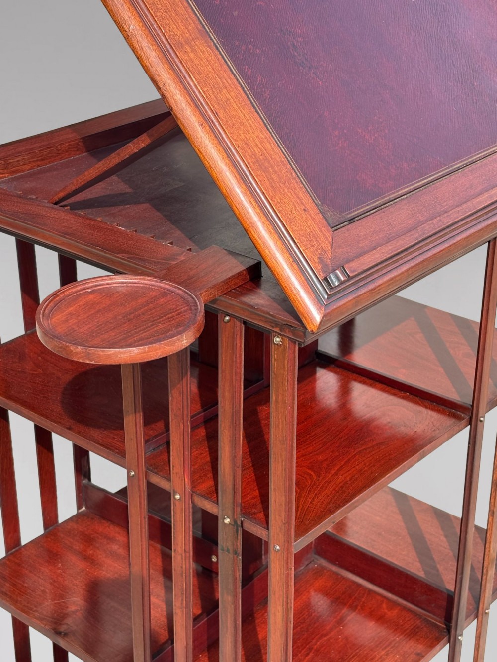 A tall nineteenth-century mahogany revolving bookcase featuring open slatted sides, tiered shelving, pull-out circular trays, and an angled reading slope with a burgundy leather surface. View VIII