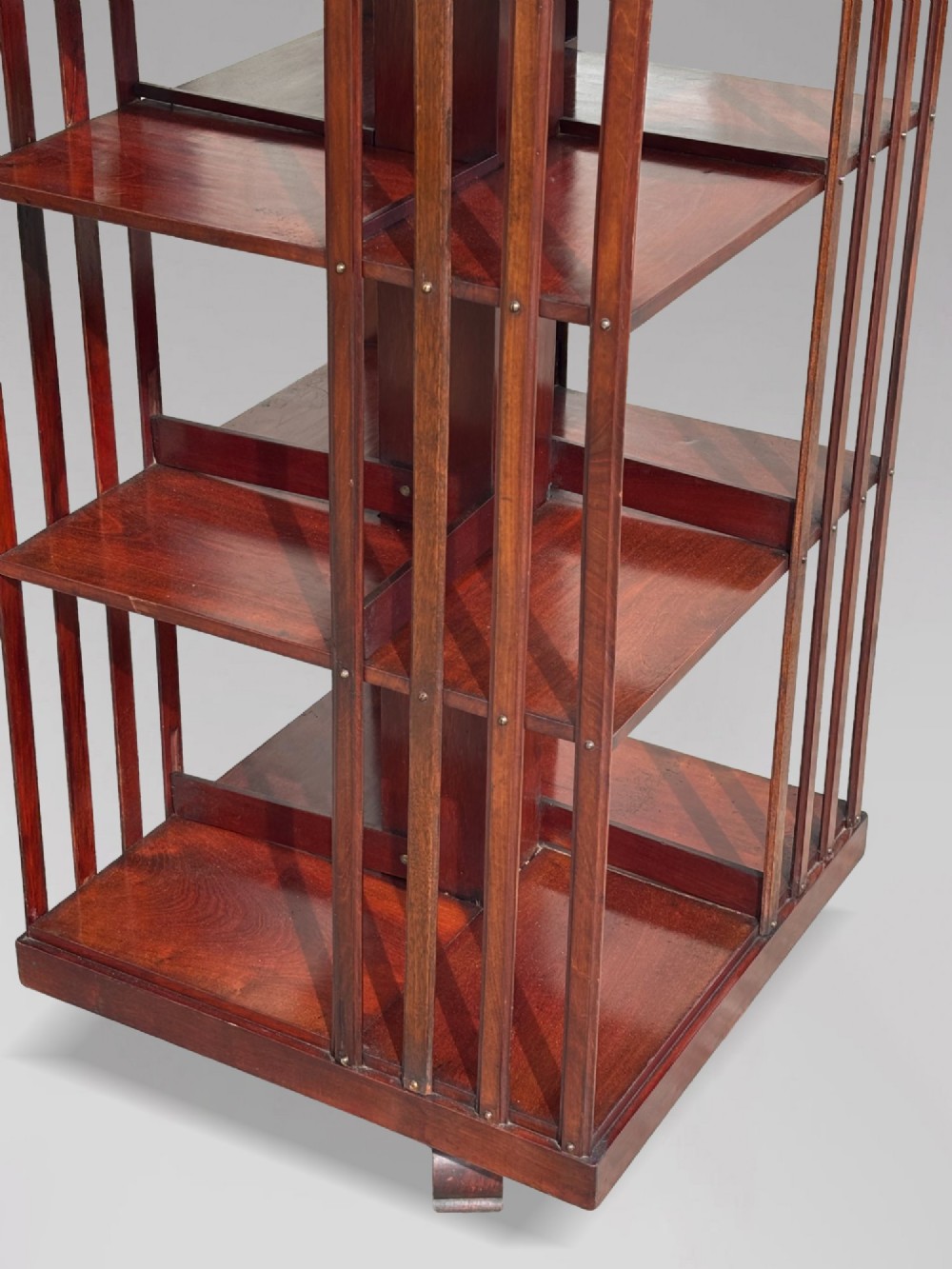 A tall nineteenth-century mahogany revolving bookcase featuring open slatted sides, tiered shelving, pull-out circular trays, and an angled reading slope with a burgundy leather surface. View IX