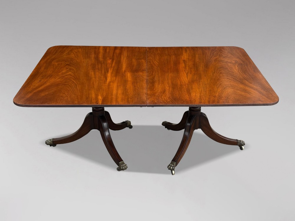 An early 19th-century Georgian mahogany twin pedestal dining table with a removable extension leaf, turned support pillars, and splayed legs ending in brass toe castors. View IV