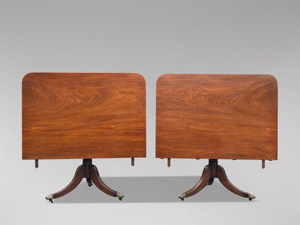 An early 19th-century Georgian mahogany twin pedestal dining table with a removable extension leaf, turned support pillars, and splayed legs ending in brass toe castors. View V