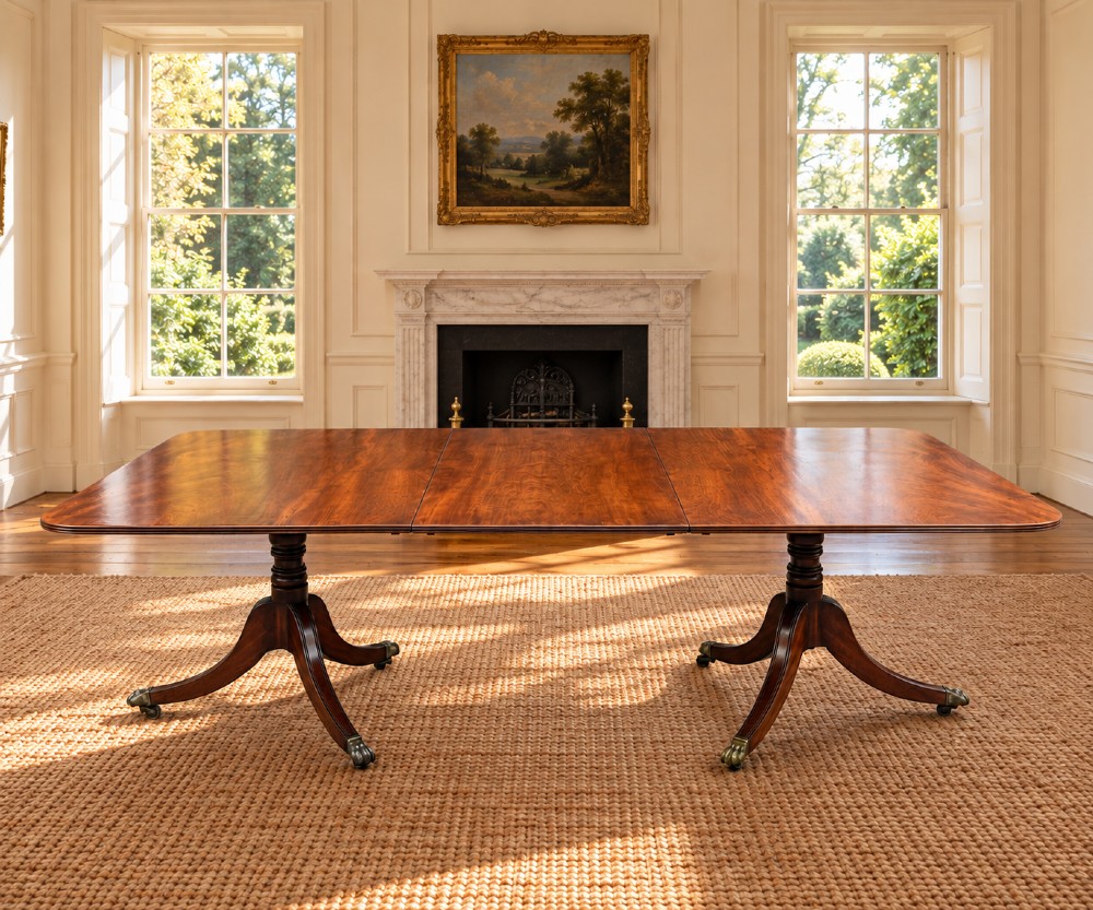 An early 19th-century Georgian mahogany twin pedestal dining table with a removable extension leaf, turned support pillars, and splayed legs ending in brass toe castors. View VI