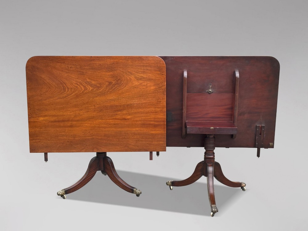 An early 19th-century Georgian mahogany twin pedestal dining table with a removable extension leaf, turned support pillars, and splayed legs ending in brass toe castors. View VII