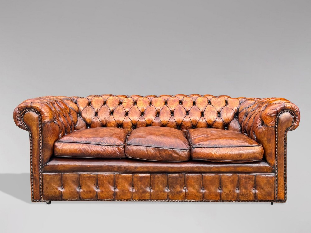 A nineteenth-century Victorian three-seater Chesterfield sofa upholstered in aged warm brown leather with deep button tufting and nailhead trim.