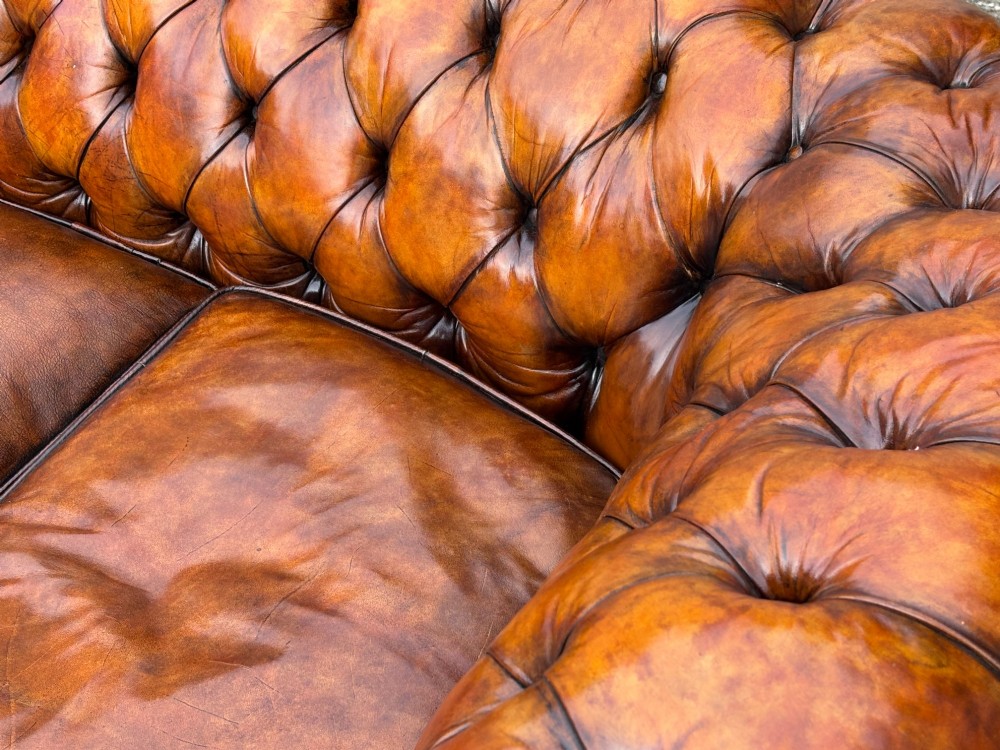 A nineteenth-century Victorian three-seater Chesterfield sofa upholstered in aged warm brown leather with deep button tufting and nailhead trim. View V