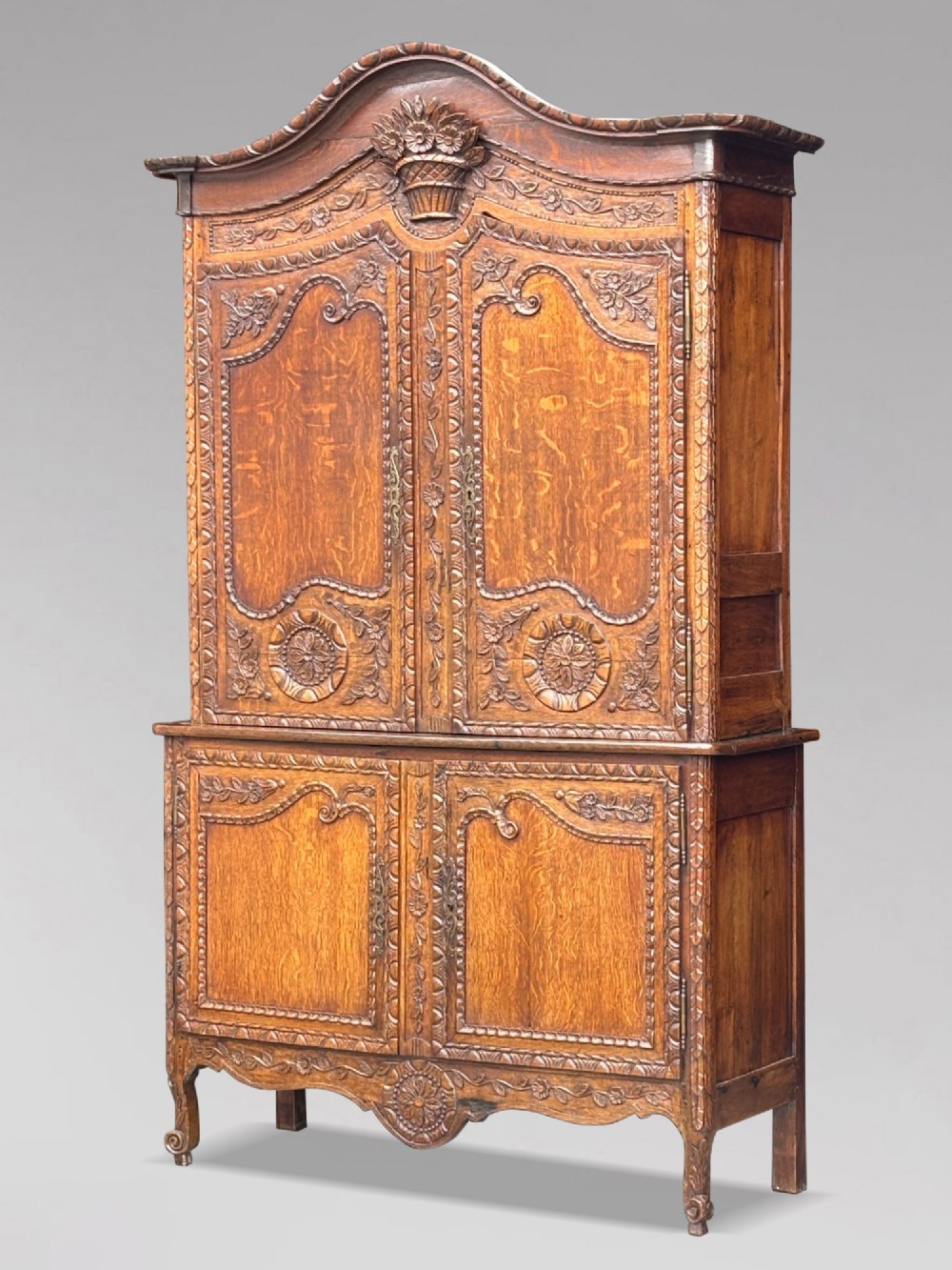 An 18th-century French Louis XVI carved oak buffet deux corps featuring two upper panelled doors topped with a floral basket carving above a two-door base resting on short scrolled feet.