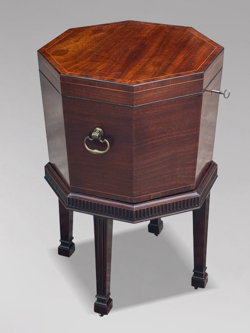 An eighteenth-century octagonal mahogany wine cooler featuring brass side handles, a keyhole detail, boxwood inlay, and fluted legs on castors.