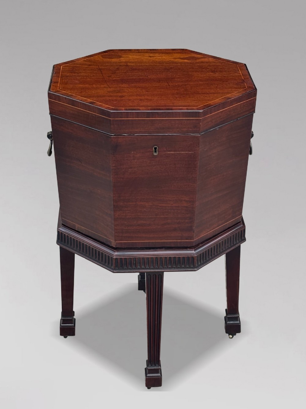 An eighteenth-century octagonal mahogany wine cooler featuring brass side handles, a keyhole detail, boxwood inlay, and fluted legs on castors. View II