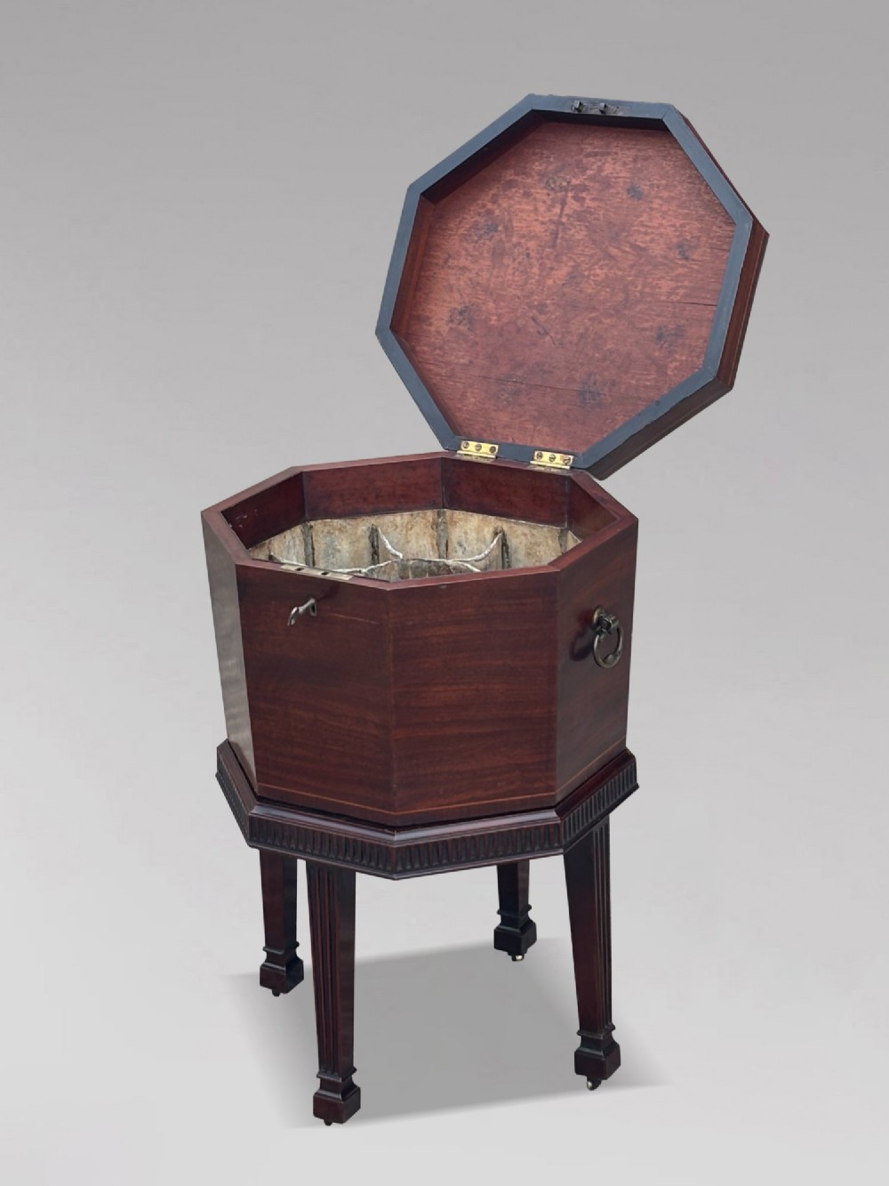 An eighteenth-century octagonal mahogany wine cooler featuring brass side handles, a keyhole detail, boxwood inlay, and fluted legs on castors. View IV