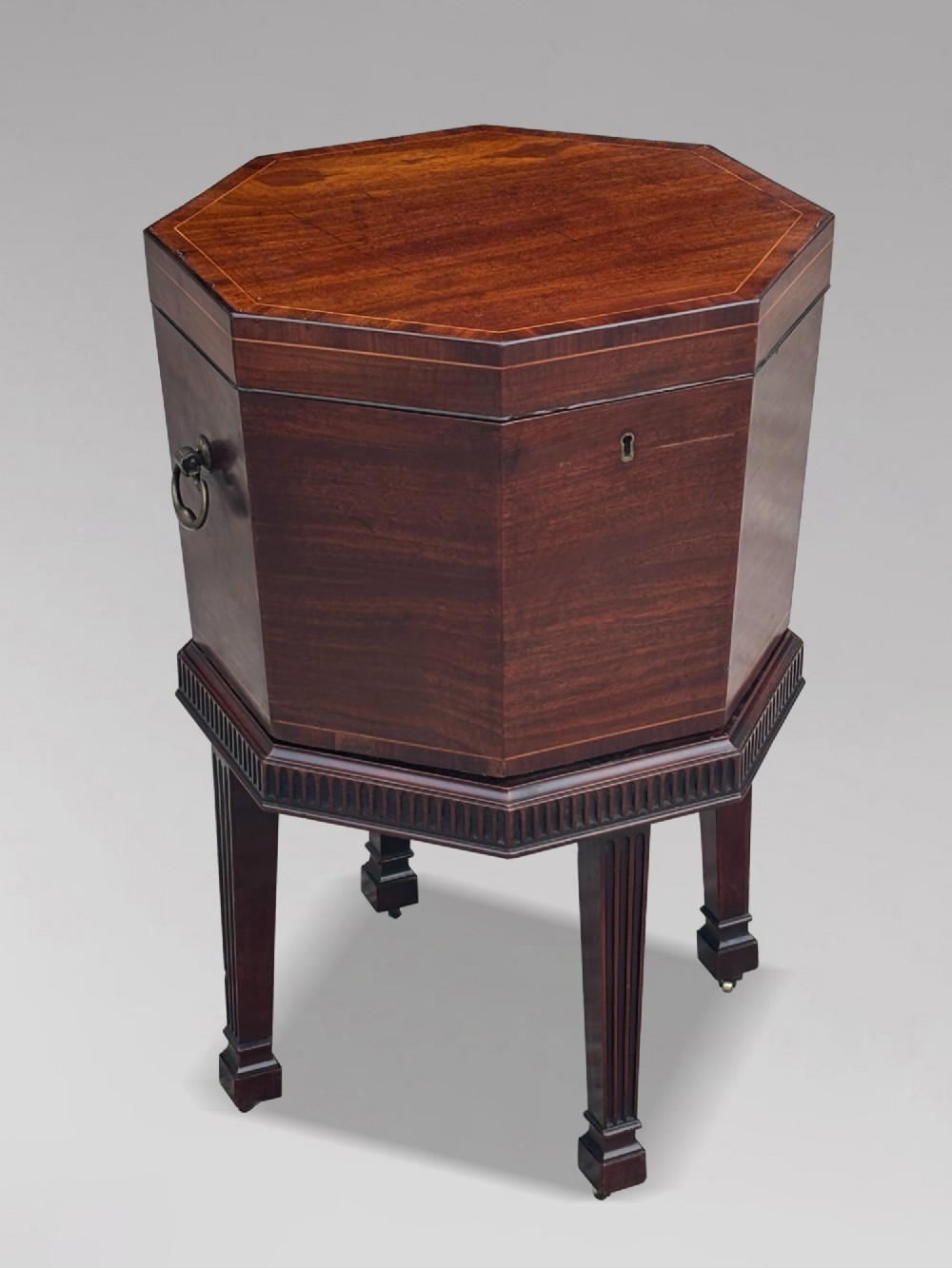 An eighteenth-century octagonal mahogany wine cooler featuring brass side handles, a keyhole detail, boxwood inlay, and fluted legs on castors. View XII