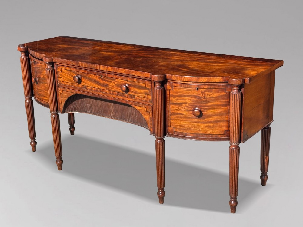 An antique 19th-century William IV mahogany sideboard featuring reeded fluted legs, line inlay, and a central drawer above an arched recess. View III