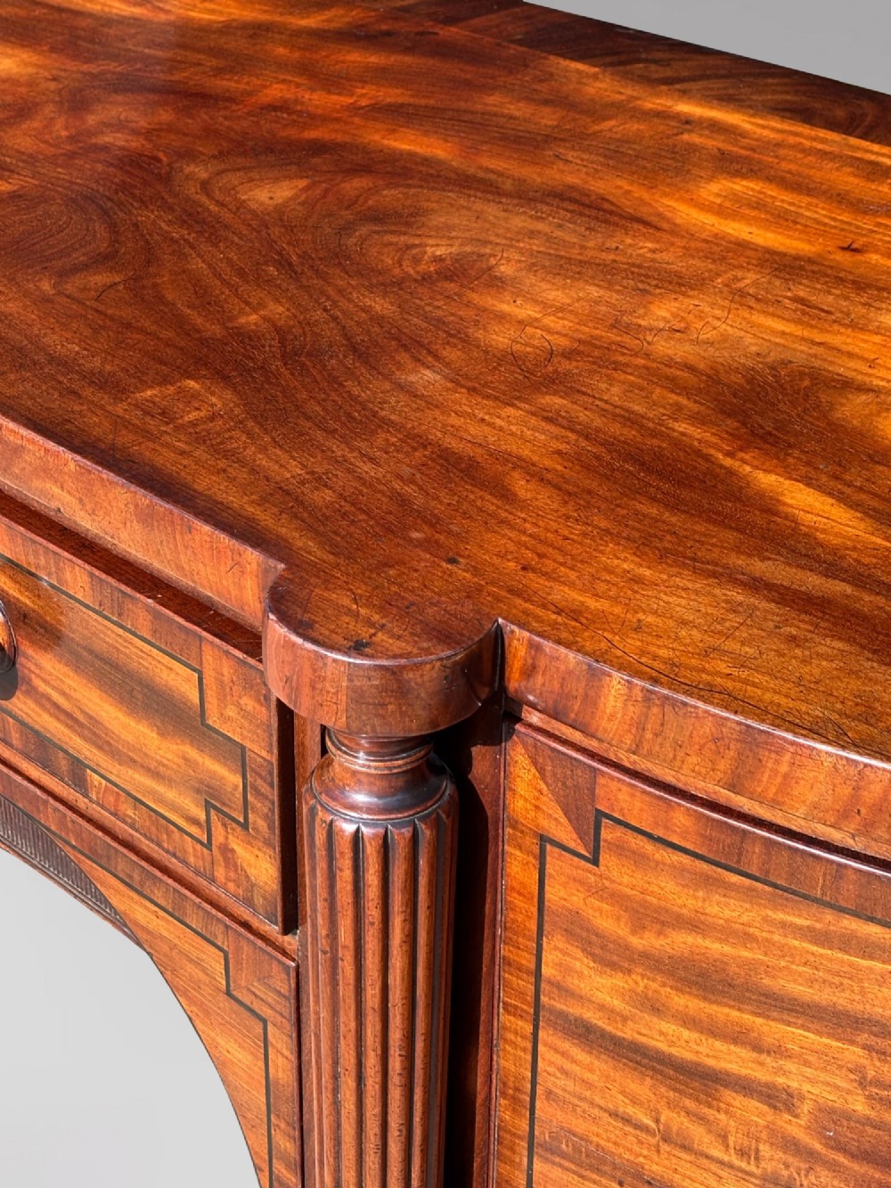 An antique 19th-century William IV mahogany sideboard featuring reeded fluted legs, line inlay, and a central drawer above an arched recess. View IV