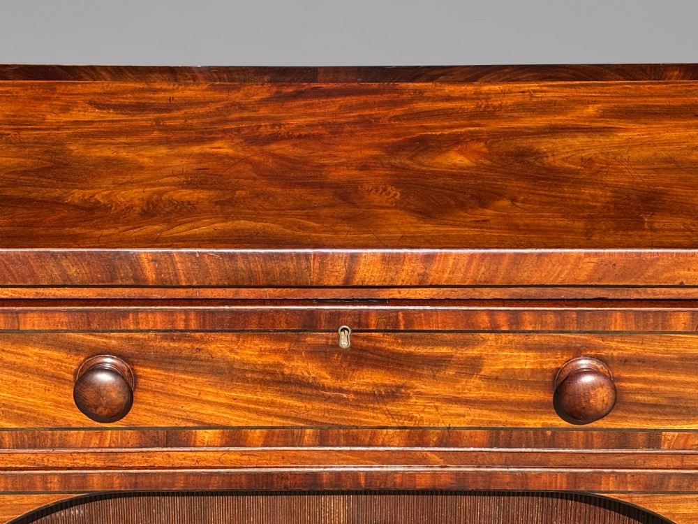 An antique 19th-century William IV mahogany sideboard featuring reeded fluted legs, line inlay, and a central drawer above an arched recess. View V