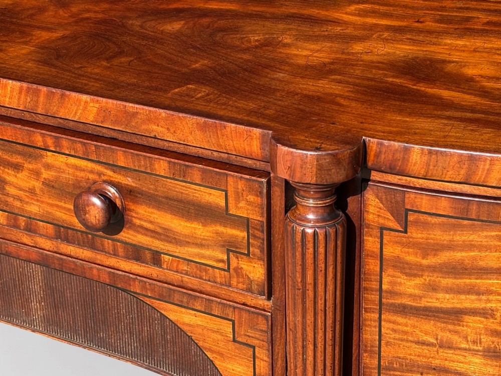 An antique 19th-century William IV mahogany sideboard featuring reeded fluted legs, line inlay, and a central drawer above an arched recess. View VI
