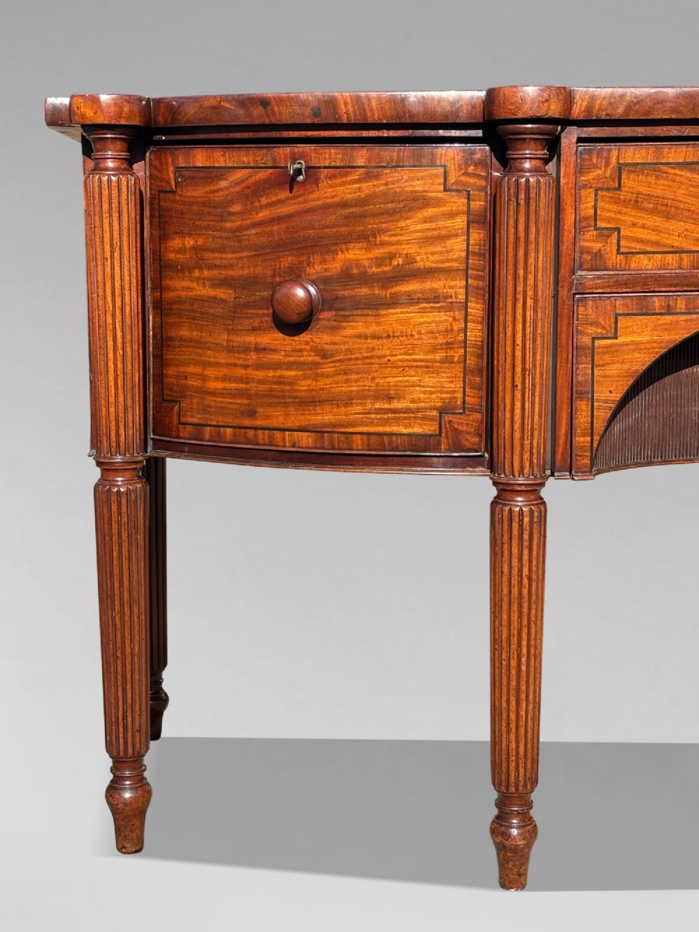 An antique 19th-century William IV mahogany sideboard featuring reeded fluted legs, line inlay, and a central drawer above an arched recess. View VII